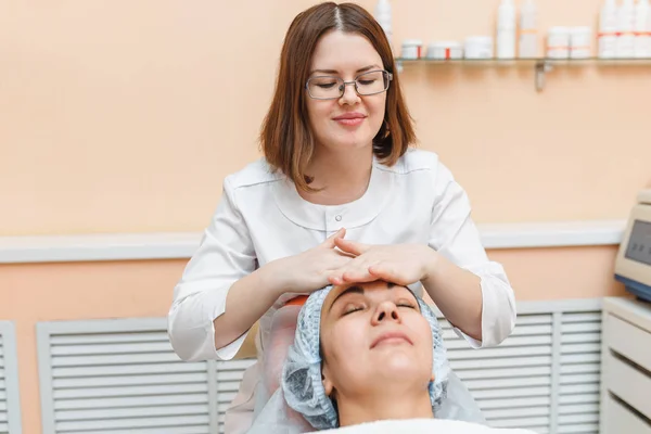 Uma médica em uma clínica de cosmetologia massagens e limpa o rosto do cliente, preparando-a para o procedimento de beleza — Fotografia de Stock