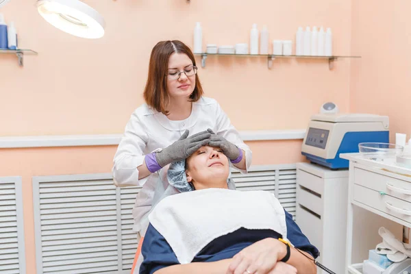 Mulher médico fazendo massagem facial com luvas elétricas na clínica de cosmetologia — Fotografia de Stock