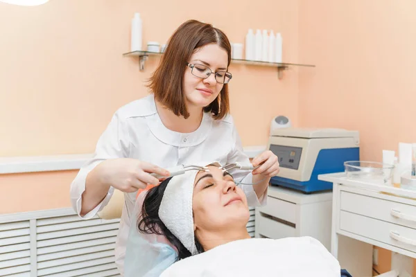 Terapeuta aplicando tratamiento cosmético de belleza galvánica de baja frecuencia a la mujer en la clínica de cosmetología —  Fotos de Stock