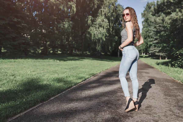 Молодая привлекательная женщина в сексуальных джинсах позирует в летнем парке — стоковое фото