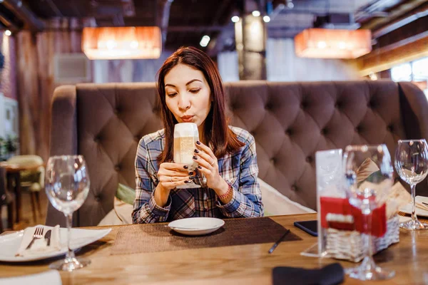 Beautiful young brunette eastern woman sitting in cafe and drinking latte coffee — Stock Photo, Image