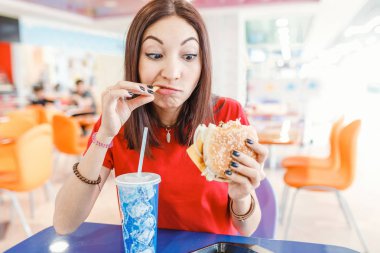 Hamburger, soda içmek ve patates kızartması fast food Restoran sahip mutlu genç kadın