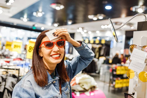 Счастливая восточная женщина покупает и выбирает стильные солнцезащитные очки в магазине в Мэлл — стоковое фото