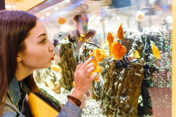 Усміхнена молода брюнетка дивиться на рибу в акваріумі — стокове фото