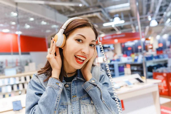 Happy eastern woman testing new headphones in the electronics shop