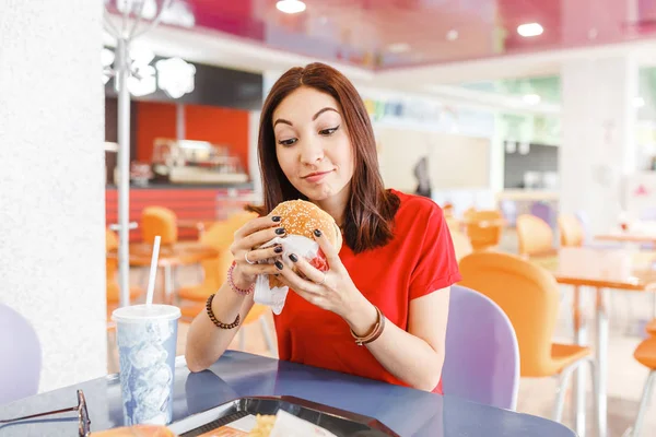 Ευτυχισμένος υγιή γυναίκα κάθεται στο εσωτερικό δικαστήριο τροφίμων και τρώει ένα νόστιμο χάμπουργκερ, σύγχρονη γεύμα έννοια — Φωτογραφία Αρχείου