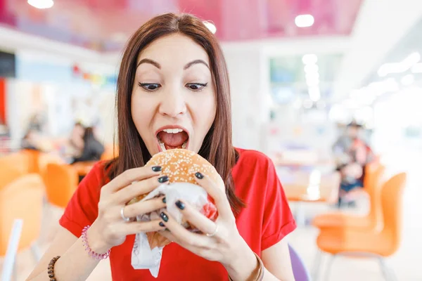 Здорова молода жінка кусає гамбургер у фаст-фуді — стокове фото