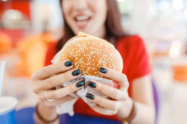 Glückliche gesunde Frau sitzt im Innenhof Food Court und isst einen leckeren Hamburger, modernes Mahlzeitkonzept — Stockfoto