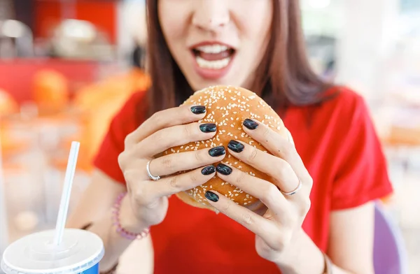 Досить молода смішна жінка їсть гамбургер всередині ресторану швидкого харчування — стокове фото