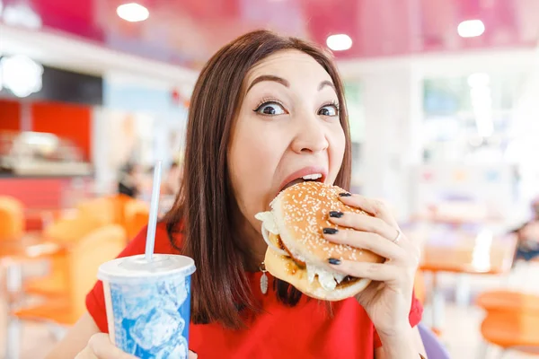 Досить молода смішна жінка їсть гамбургер всередині ресторану швидкого харчування — стокове фото
