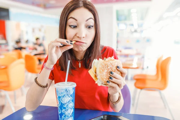 Mujer joven feliz teniendo hamburguesa, bebida de soda y papas fritas en restaurante de comida rápida — Foto de Stock