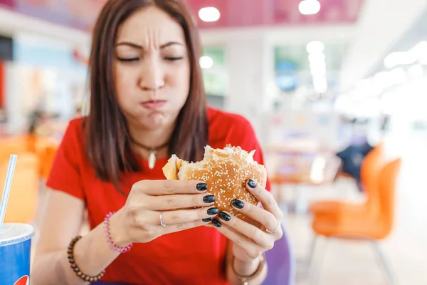 Vrouw met hamburger in de hand, waardoor slecht en walgelijk gezicht, concept van het slechte bedorven voedsel en problemen met de spijsvertering — Stockfoto