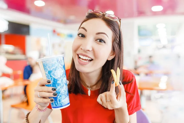 Happy young woman having hamburger, soda drink and french fries in fast food restaurant