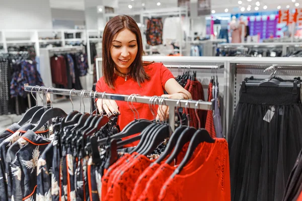 Mujer eligiendo ropa elegante durante las compras en la tienda boutique en el centro comercial — Foto de Stock