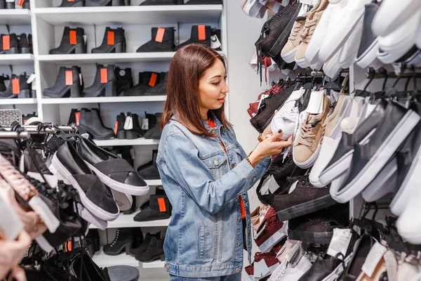 Feliz cliente joven mujer elegir par de zapatillas de deporte zapatos y comprarlo en la tienda de ropa, concepto de compras casuales — Foto de Stock