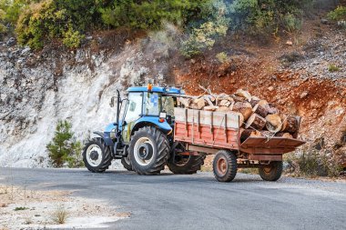 Traktör ahşap günlükleri ve dağlarda bir asfalt yolda parçaları ile