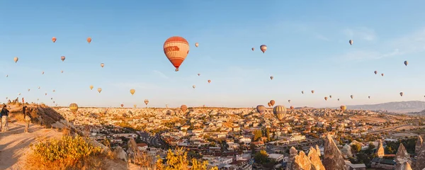 Touristenmassen beobachten vom Aussichtspunkt aus den Heißluftballon, der über die Felsenlandschaft in Kappadokien fliegt — Stockfoto