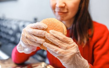 Kadının modern fastfood restoranda hamburger elinde eldiven eller