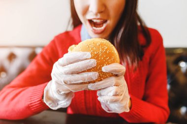 Mutlu genç kadın kapalı cafede koruyucu beyaz eldivenler, hamburger yemek