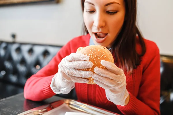Kvinnans händer i handskar håller burger i moderna fastfood restaurang — Stockfoto