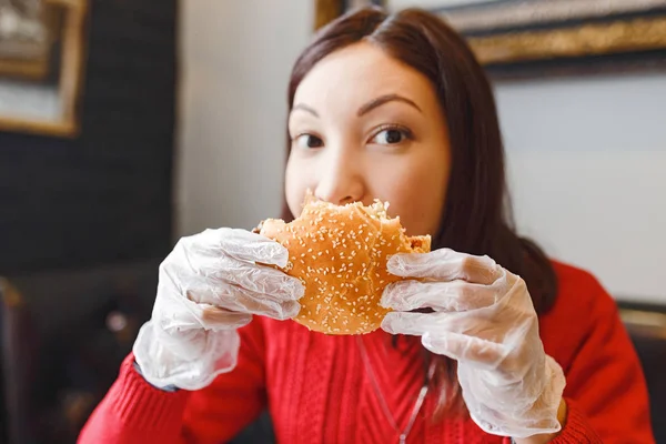 Жіночі руки в рукавичках тримають бургер в сучасному ресторані швидкого харчування — стокове фото