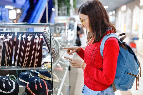Aziatische hipster vrouw kiest sieraden in een winkel en kijkt naar de vitrine — Stockfoto