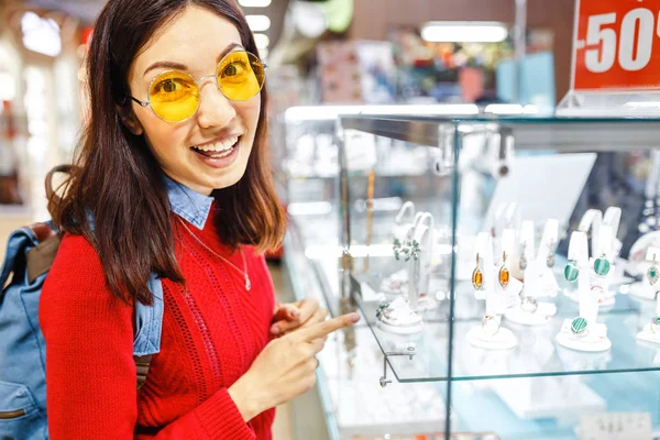Mujer hipster asiática elige joyas en una tienda y mira la vitrina —  Fotos de Stock