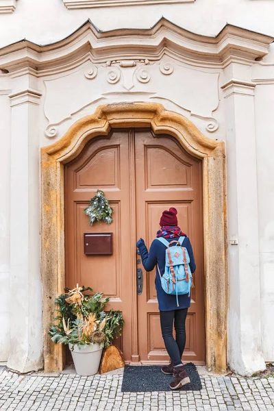Žena Turistický batoh klepe na dveře hotelu krásně zdobené nový rok s vánoční věnec — Stock fotografie