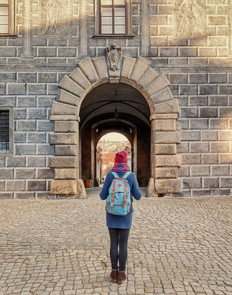 Женщина-туристка в пальто с рюкзаком путешествует по старым улицам города Чески Крумлов, концепция отпуска в Европе — стоковое фото