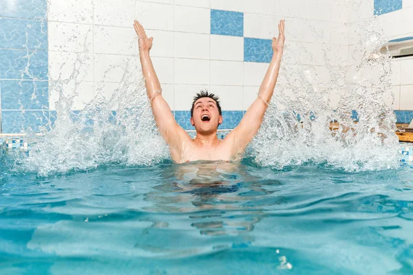 Uomo gioioso nuota in piscina e facendo un mucchio di spruzzi d'acqua — Foto Stock