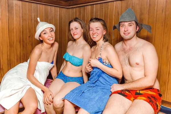 A happy group of men and women rest and relax in a steam Finnish sauna, the concept of entertainment for a company of young people in the bath complex — Stock Photo, Image