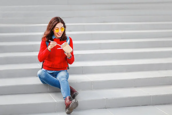 Щаслива дівчина їсть азіатську швидку їжу з паперової коробки на вулиці міста, концепція студентської або робочої обідньої перерви — стокове фото