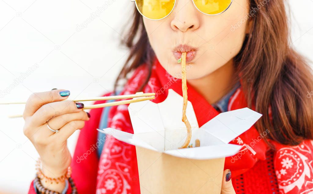 Bright hipster woman eating asian fast food from takeaway box with chop sticks, Wok noodles concept