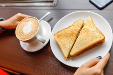 Sandviç ve kahve beyaz Kupası tahta masada Kahvaltı sabah kafede tutan el