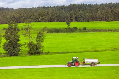Tractor with fertilizer tank rides on a country road in a green field. Agriculture and farming concept