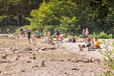 08 Ağustos 2019, Schwangau, Almanya: Aileler Neuschwanstein kalesi yakınlarındaki bir dağ nehrinin kıyısında dinleniyor
