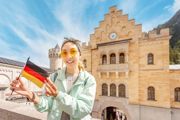 Szczęśliwa Azjatka z niemiecką flagą cieszy się pięknym widokiem na magiczny zamek Neuschwanstein wysoko w Alpach Bawarskich. Koncepcja podróży i wakacji — Zdjęcie stockowe