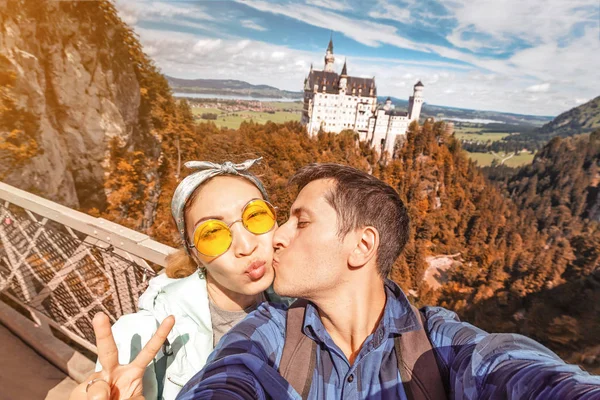 Een gelukkig Aziatisch meisje en een Europese reiziger omarmen en kussen tijdens hun huwelijksreis op de achtergrond van het beroemde Neuschwanstein kasteel. — Stockfoto