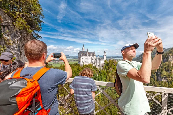 08 August 2019, Schwangau, Germany: Crowds of tourists take photos and selfies on their smartphones on the Maria bridge overlooking the popular Neuschwanstein castle — Stock Photo, Image