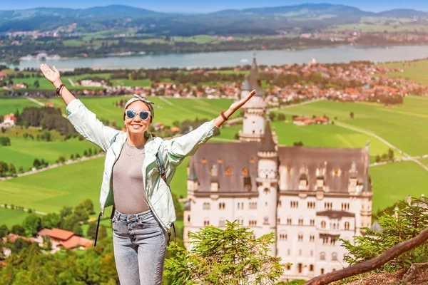 Szczęśliwa dziewczyna rozłożyła ramiona na tle słynnego i wspaniałego zamku Neuschwanstein w Bawarii. Atrakcje turystyczne w Niemczech i Europie — Zdjęcie stockowe