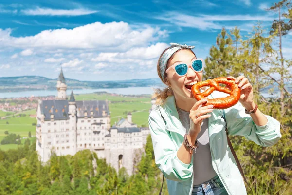 행복 한 아시아 여행자 소녀는 전설적 인 네우스 청교도의 성 뒤에서 바삭 한 프레첼을 먹는다. 바이에른의 관광 개념 — 스톡 사진