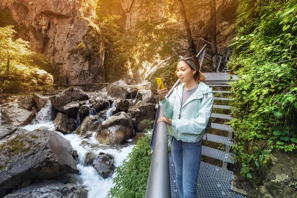 Šťastná asijská turistka kráčí podél železné stezky podél strmých útesů v kaňonu řeky Pollat v bavorských Alpách — Stock fotografie