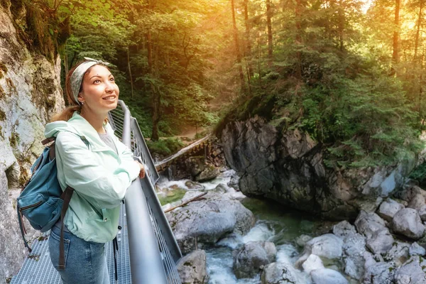 Happy asian tourist girl walk along a hinged iron trail along sheer cliffs in the canyon of the Pollat river in the Bavarian Alps