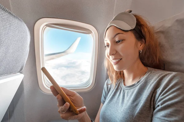 Asian woman using mobile internet at the background of the window with airplane wing — Stock Photo, Image