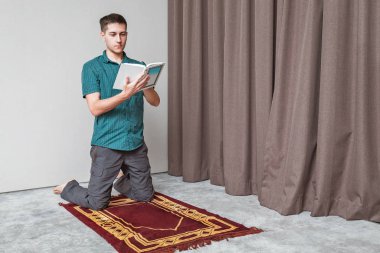Genç bir adam içteki küçük portatif bir halının üzerinde Kuran okuyup namaz kılıyor. Din ve ritüel kavramı