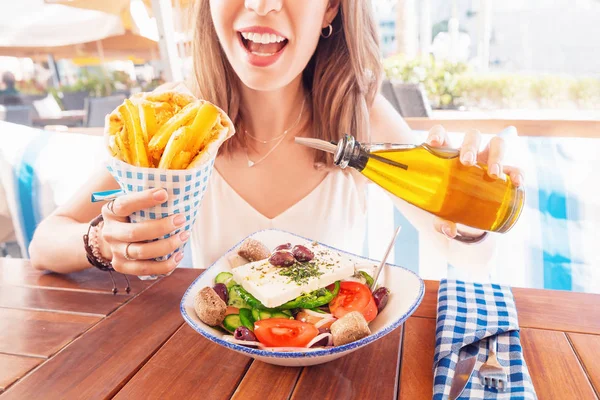 Cheerful tourist girl tries Greek cuisine at a local restaurant. On the table traditional salad Horiatiki and Gyros in Pita — Stock Photo, Image