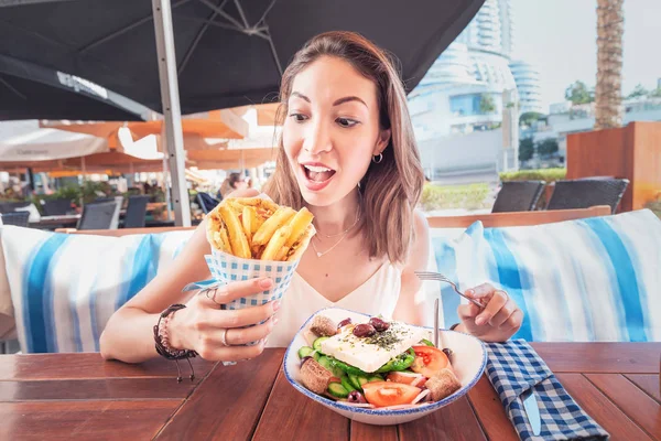 Cheerful tourist girl tries Greek cuisine at a local restaurant. On the table traditional salad Horiatiki and Gyros in Pita — Stock Photo, Image