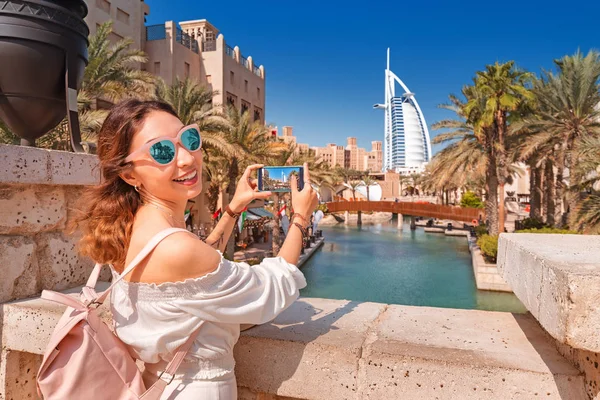 27 November 2019, UAE, Dubai: happy girl takes a photo on her smartphone against the backdrop of the cityscape in Dubai with the hotel Burj al Arab — 스톡 사진