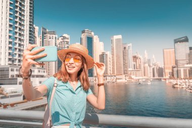 Happy Asian tourist girl takes selfie photos in popular Marina district in Dubai for her social media and blog