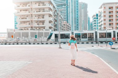A woman in a modern neighborhood with high-rise buildings goes to the tram stop. Urban transport and passenger and lifestyle concept